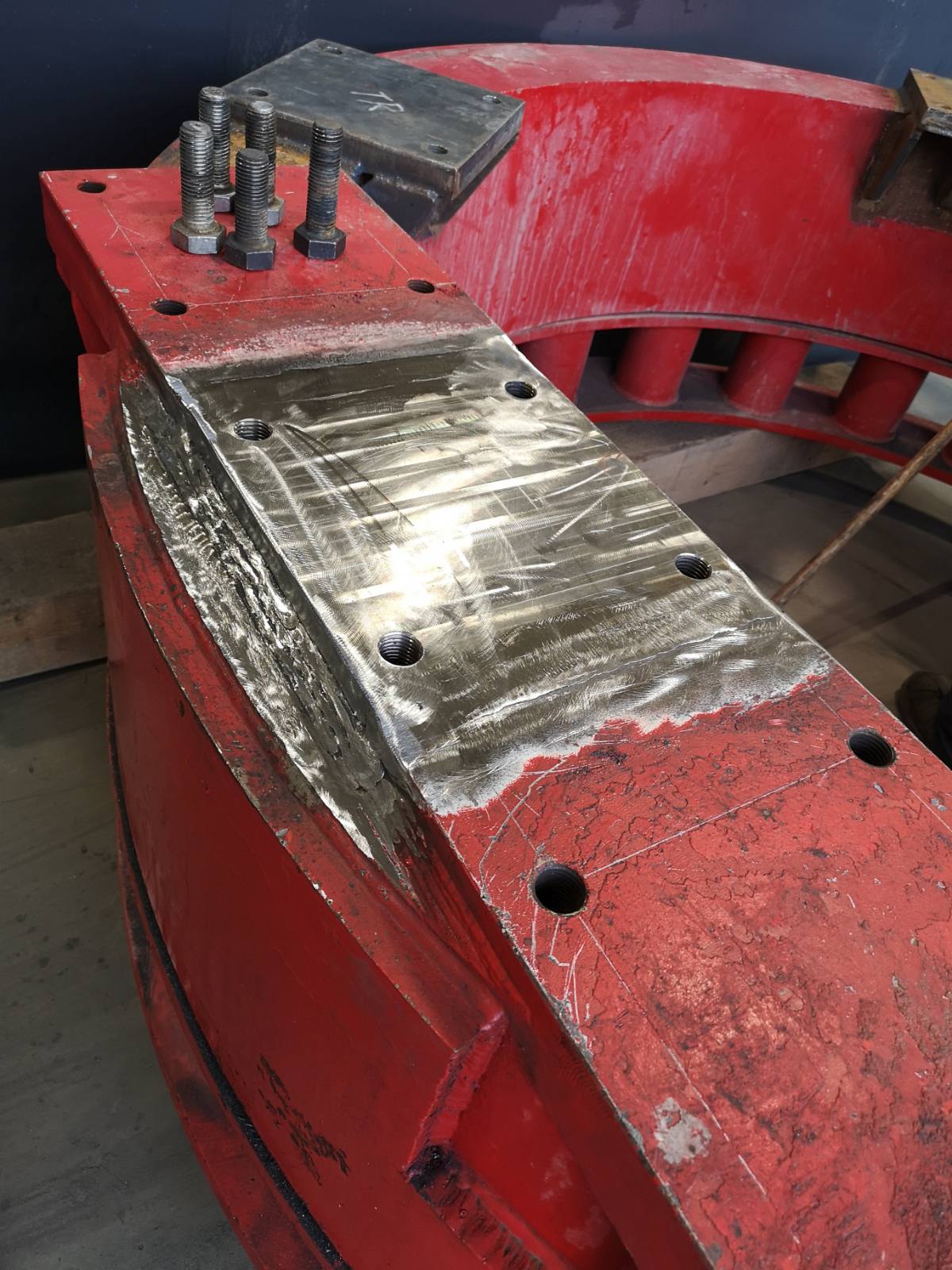 lose-up of a red industrial steel component with a machined surface and bolt holes prepared for welding and reassembly, Cambridge fabrication services