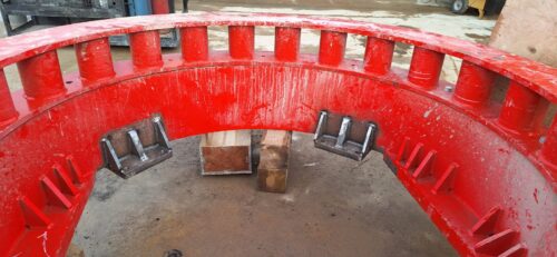 Close-up of a large red industrial steel structure with reinforced weld joints and support brackets, showcasing precision fabrication and heavy-duty welding work